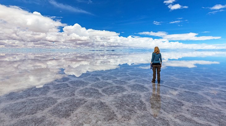 Woman gazing at reflected clouds in Salar de Uyuni, Bolivia
