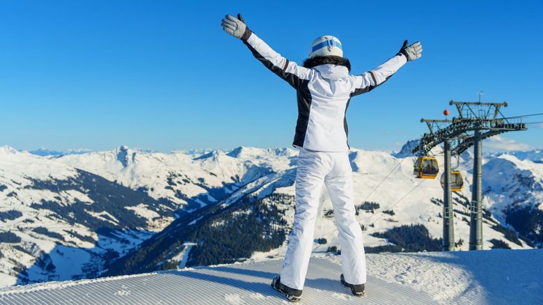 Female skier in white joyfully celebrates her successful run in the Austria Alps at Kaprun with blue skies in the background
