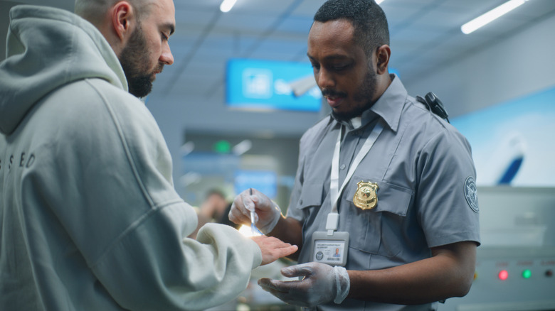 TSA agent conducts a hand swab and secondary screening while questioning a passenger at an airport security checkpoint