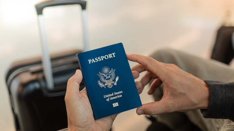 Close-up of traveler holding USA passport at the airport with suitcase beside them
