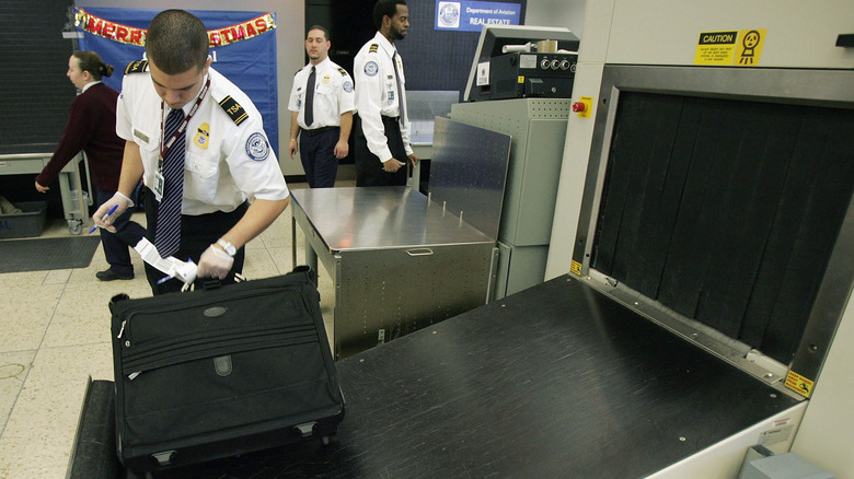 TSA worker checking a bag after passing through a screening machine
