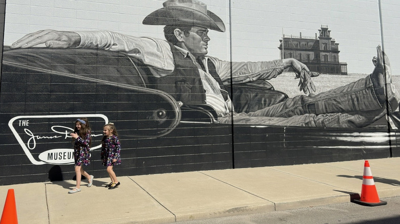 Black and white mural of James Dean painted on the side of the James Dean. Museum in Fairmount, Indiana with two little girls walking by