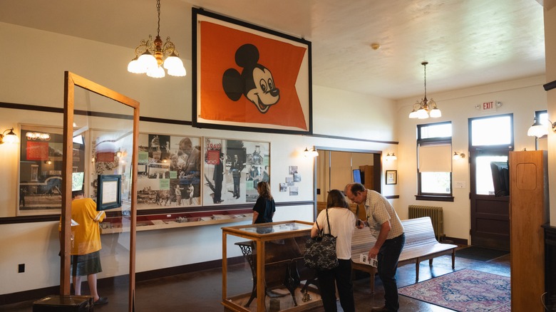 People visit the Walt Disney Hometown Museum surrounded by a Mickey Mouse flag, photos of Walt and Roy, and other memorabilia.