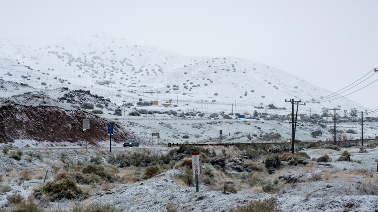 Winter view in Pearblossom, California, including snow covered hills and a car driving on an icy road
