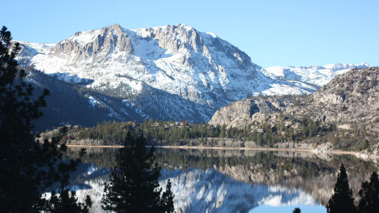 View of June Lake and snowy June Mountain, California with pine trees reflecting in the lake on a sunny day