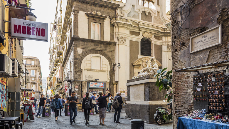 People walking in Largo Corpo di Napoli along Spaccanapoli, on the right side of the photo the roman period marble sculpture of Dio Nilo (God Nile), on the background Chiesa di Santa Maria Assunta dei Pignatelli (Baroque Style)