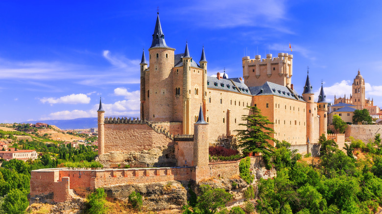 View of the imposing Alcázar de Segovia on a hillside against a brilliant blue sky