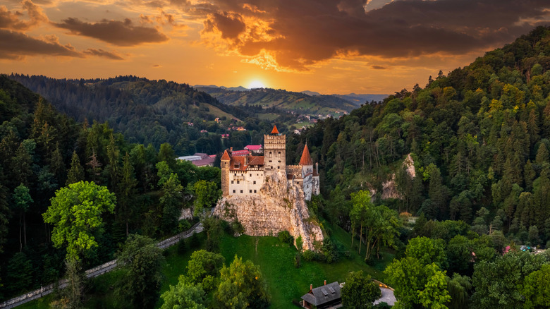 Bran Castle at sunset with an orange sky and surrounded by lush forests