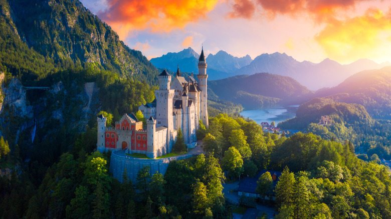 Stunning view of Bavarian mountain landscape and Neuschwanstein Castle with vibrant orange, pink, and purple sky in the background