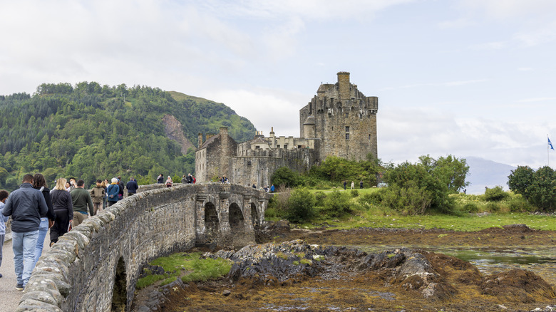 View of travelers walking on the stone bridge to access Scotland's Eilean Donan Castle on an overcast day