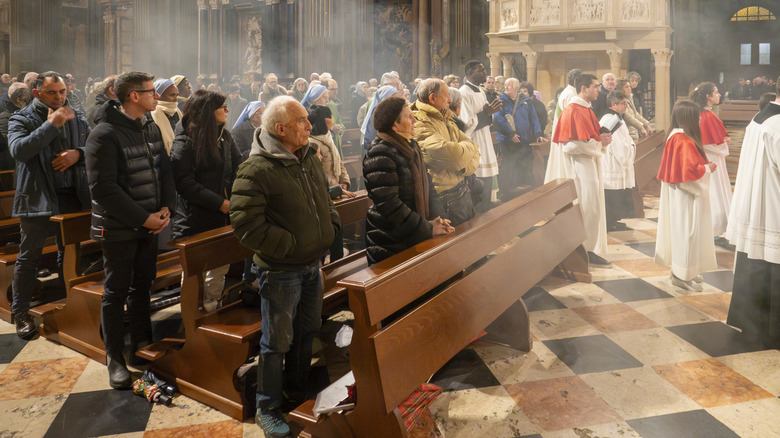 Worshippers and altar boys attending a Sunday Mass with incense smoke filling the air