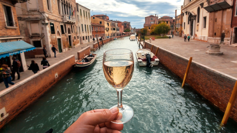 View of canals in Venice with a hand holding a glass of white wine in the foreground.