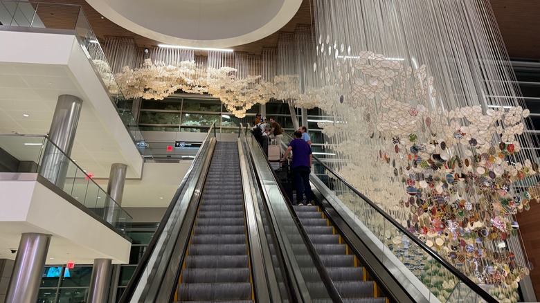 Travelers on an escalator beneath an installation by Jacob Hashimoto at Nashville International Airport