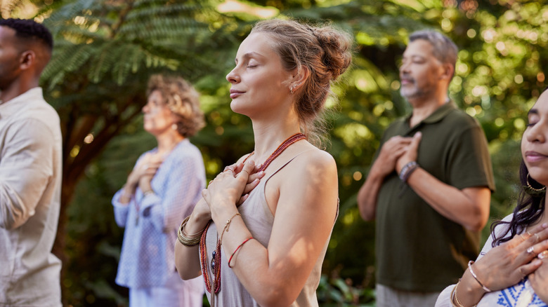 a group of people practicing yoga hold their hands to their chests with their eyes closed