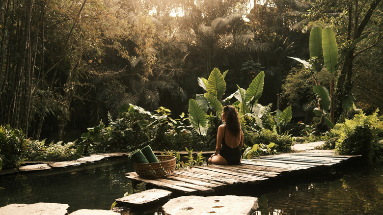 traveler in bathing suit sitting on dock in the jungle with faint glowing sunlight