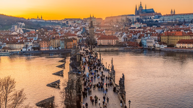 Aerial view of a crowded Charles Bridge crossing the Vltava River to Prague Castle at sunset