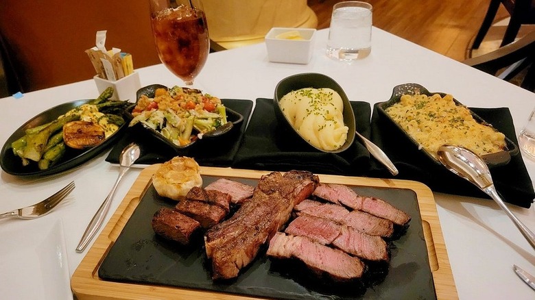 slab of steak with assorted sides on white cloth table