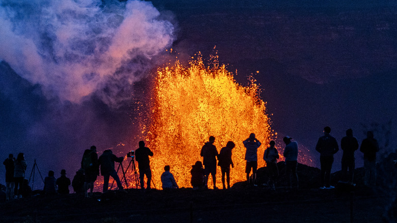 people watch as lava erupts from the mouth of the volcano