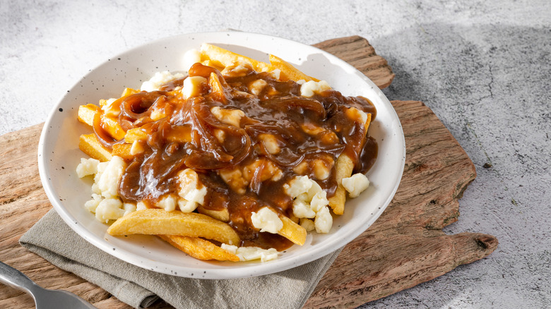 a plate of poutine on wooden cutting board