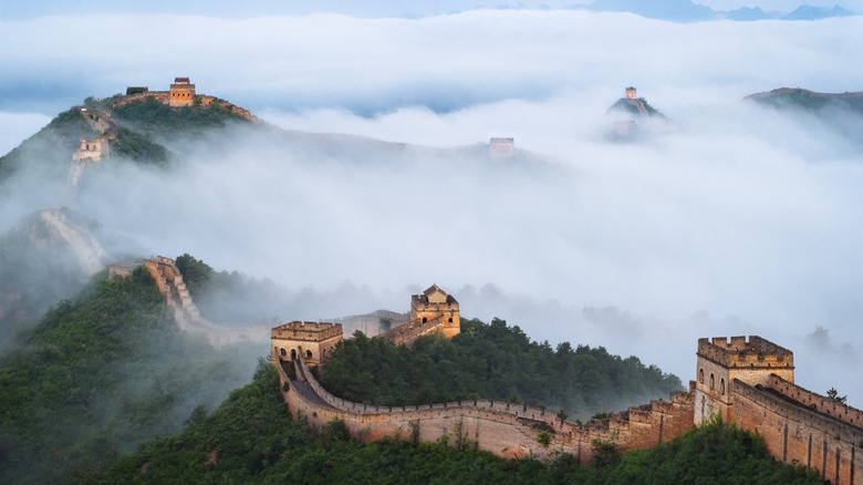 The Great Wall of China snakes over lush green mountains on a foggy day