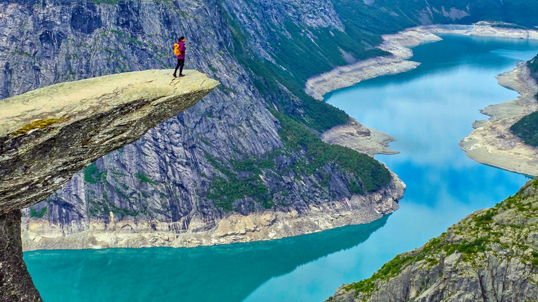 Person with orange backpack standing on the edge of Norway's Troll Tongue rock over a fjord