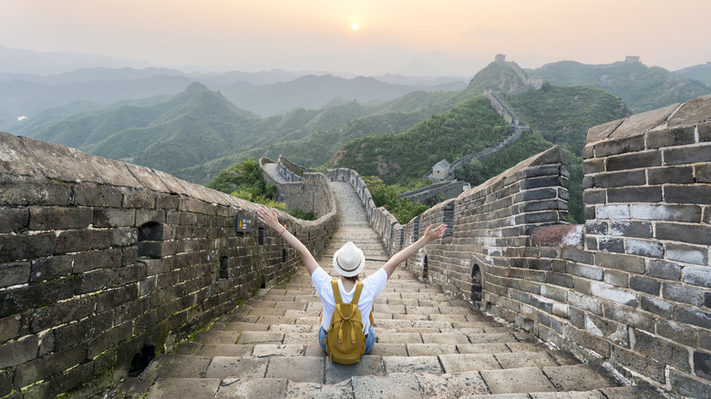 Woman sitting on top of a section of the Great Wall of China on a partly cloudy day at dusk