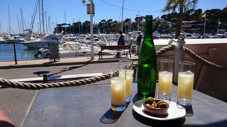 four glasses of the classic pastis on a table outside with boats on the water in background