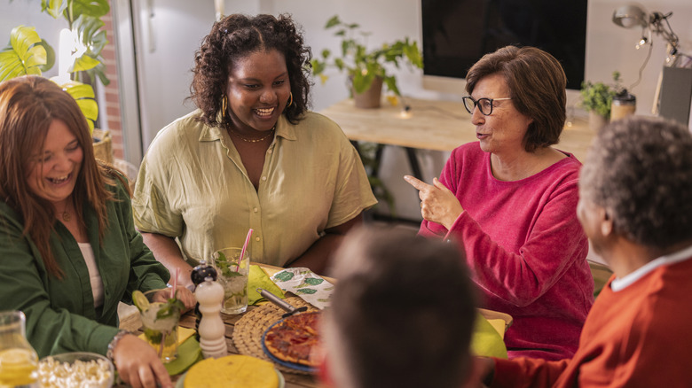 a group of people sitting at a dining table conversing and sharing a meal