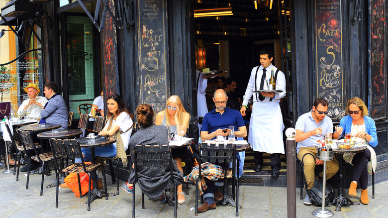 waiter carrying a tray with wine at a restaurant with terrace seating