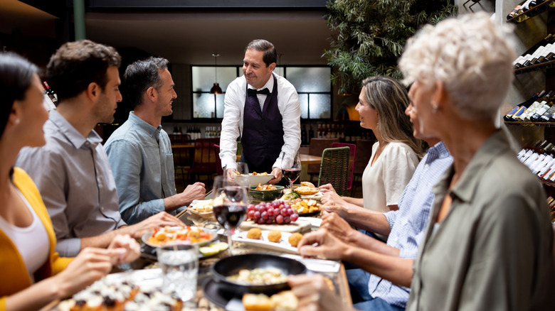 waiter serving large group of people seated at a table filled with food
