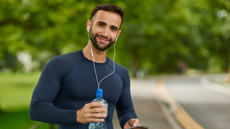 Runner wearing white headphones while holding a phone and water bottle in the park