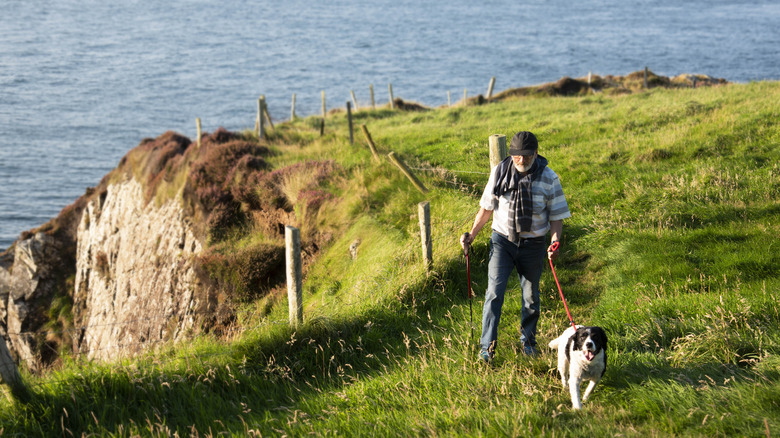 Man in layers walking his dog through the grass along the Irish coast
