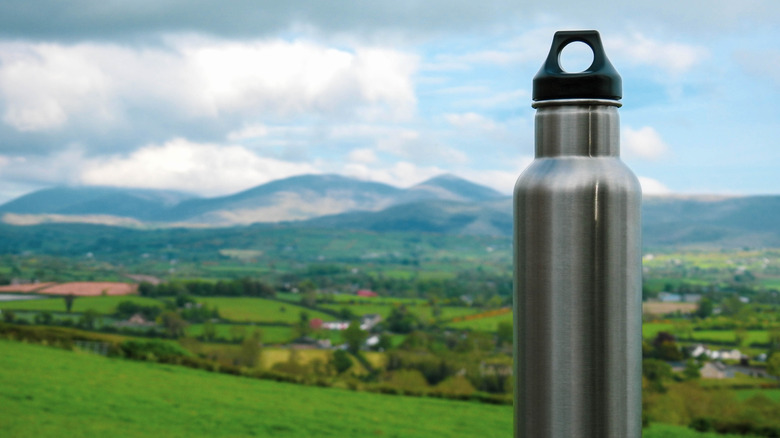 Silver water bottle propped on a fence in the lush Irish countryside