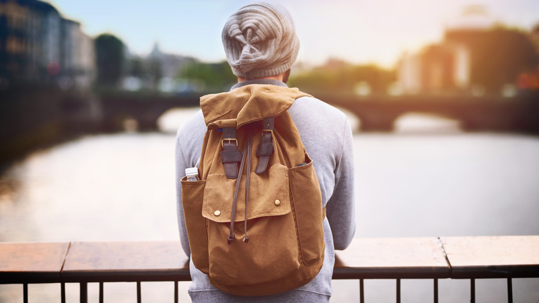 Man in hat in Dublin wearing a brown backpack looking over the river from a bridge