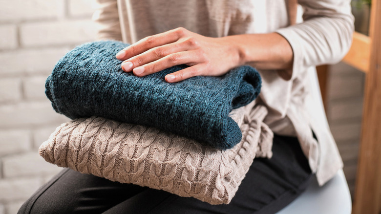 Hands holding a pile of wool sweaters