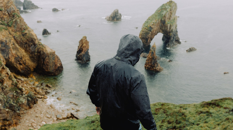 Traveler in gray hooded jacket overlooking a rocky Irish coast on a stormy day