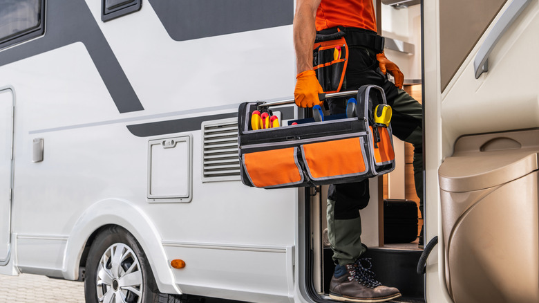 A man carrying a tool box stands in the doorway of a white and gray RV.