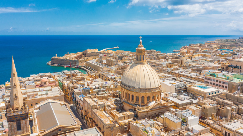 Aerial view of Valletta, Malta, with a sepia-colored church and historic buildings overlooking a blue ocean