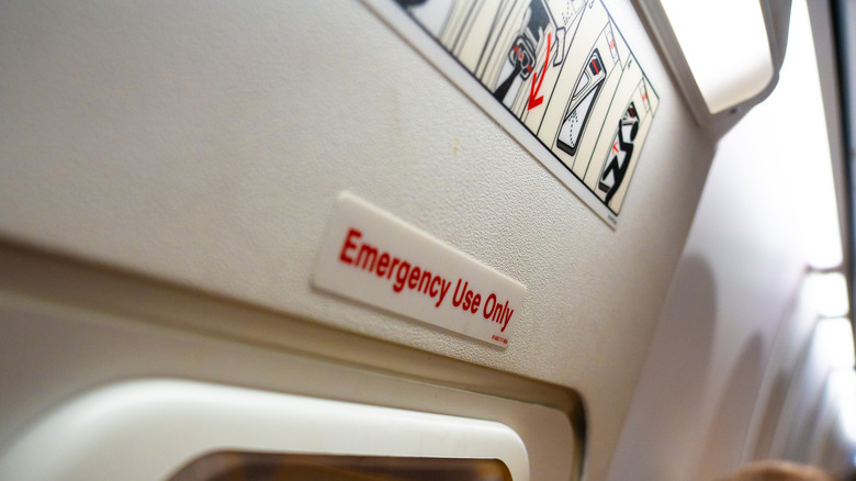 Signage marked for emergency use only is prominently displayed near the exit in an aircraft