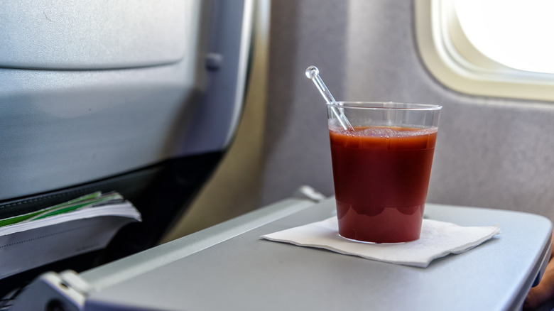 A glass of tomato juice sits on an airplane tray table.