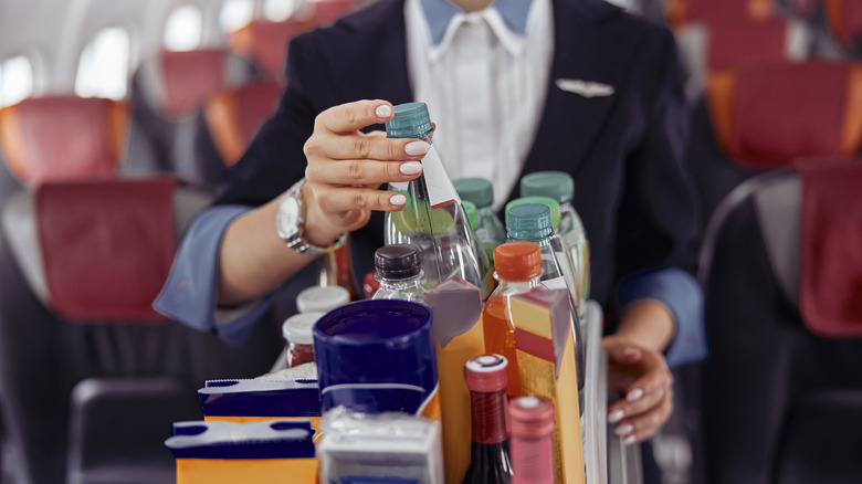 A flight attendant lifts a bottle from the top of a beverage cart during in-flight service.
