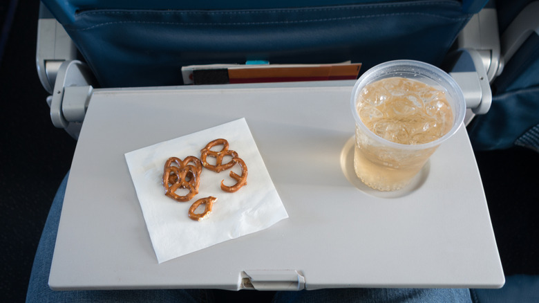A cup filled with ginger ale and ice, and some pretzels on a napkin, sitting on an airplane tray table.