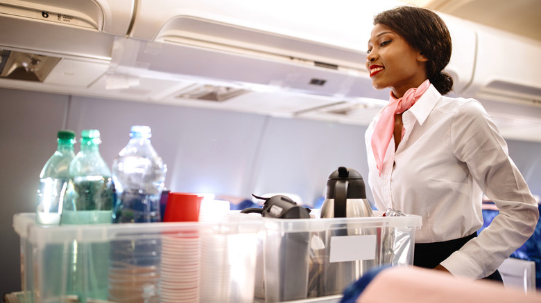 A flight attendant pushes a stocked beverage cart down the airplane aisle.