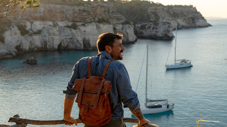 Young male tourist smiles, overlooking a picturesque bay with islands and sailboats