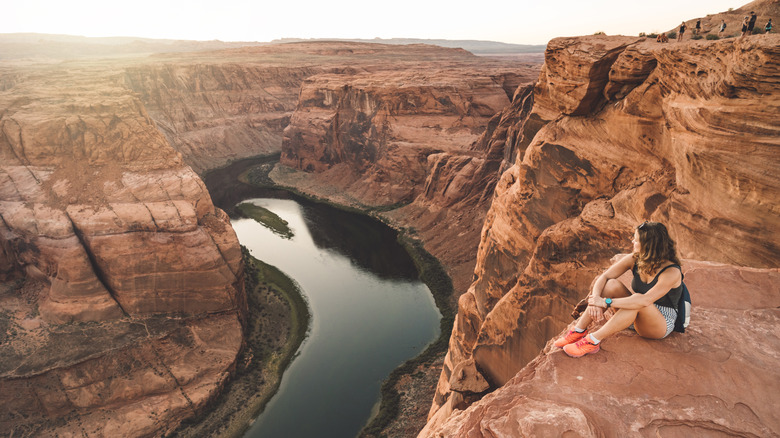 Woman sitting on a red ledge overlooking the Colorado River winding its way through the Grand Canyon