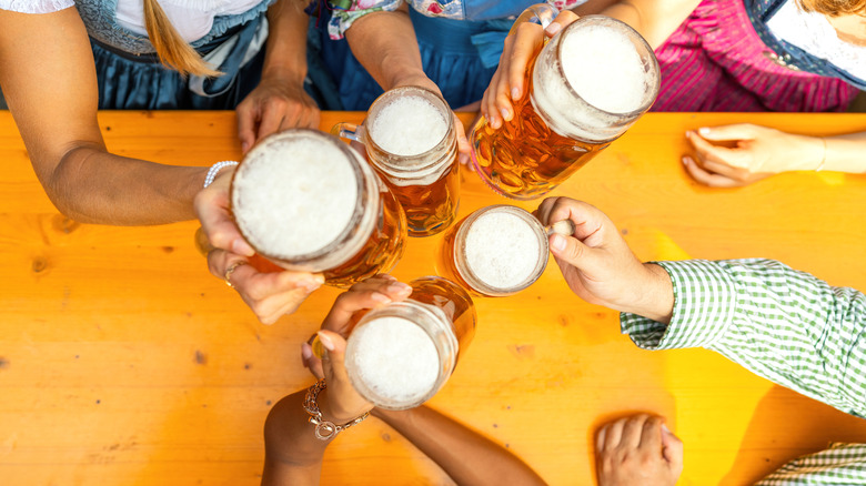 A group of people holding beer-filled glasses together over a table