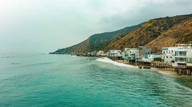 hosues on stilts built right at the ocean's edge with mountains in background