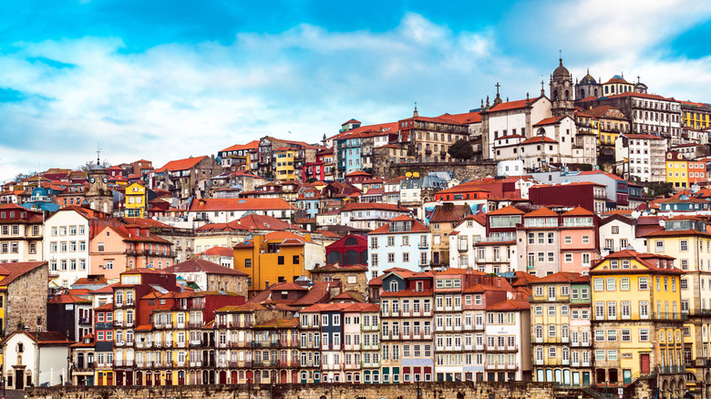 Ornate, colorful buildings appear stacked up on the streets of Porto, Portugal, leading to a tall church