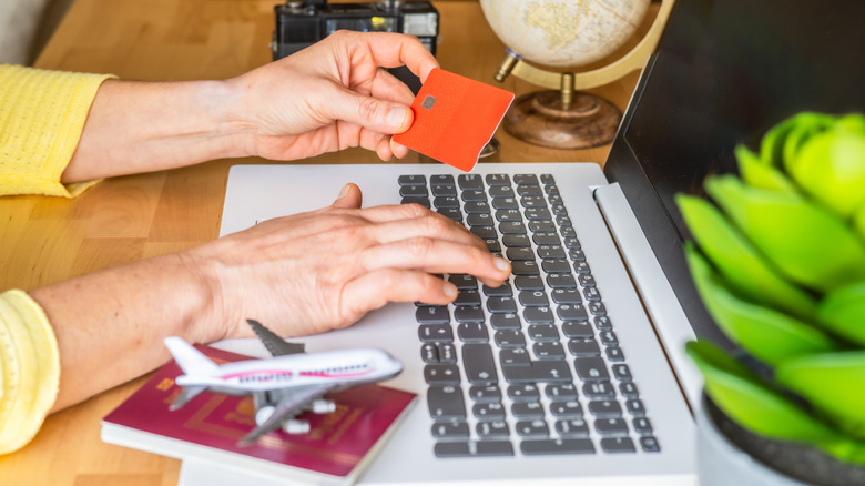 Hands holding a credit card while using a laptop, with a passport sitting to their right