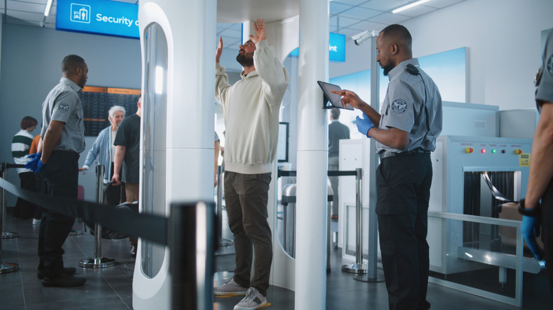 Airport security officers screening passenger in full-body x-ray machine.